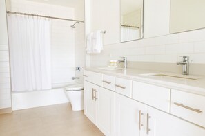 A modern bathroom with a white toilet, a shower with a curtain, a sink with a mirror above, and white cabinets. - Baltimore Place (Atlanta)
