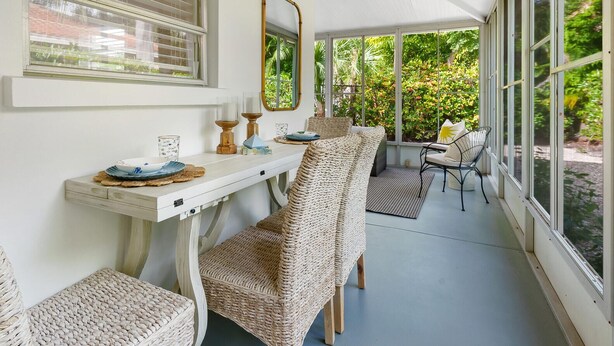 Une terrasse couverte avec une table à manger, des chaises en osier et une vue sur la verdure.