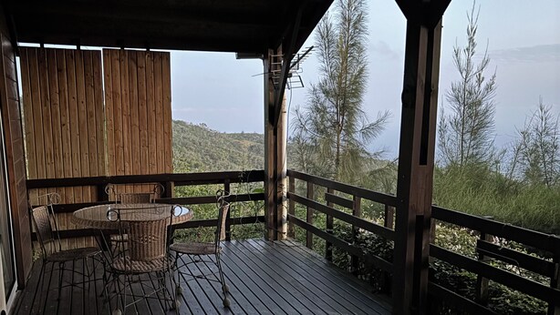 A wooden deck with a round table and chairs, overlooking a forested area. - Le NID chalet classė 3*** between sea and mountains (Les Avirons)