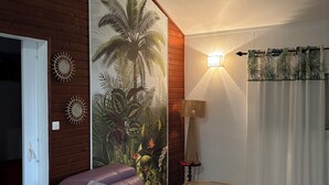 A living room with a purple sofa, a wooden coffee table, a wall-mounted lamp, and a large tropical mural. - Le NID chalet classė 3*** between sea and mountains (Les Avirons)