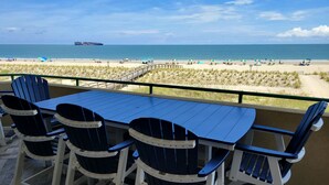 A terrace with a table and chairs overlooking a beach with umbrellas and a ship in the distance. - Desoto Beach Club 2 Tybee Vacation Rentals (Tybee Island)