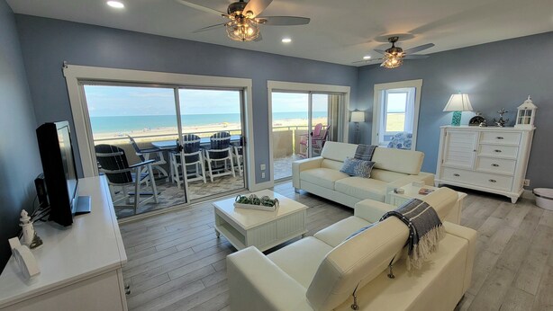 A living room with a view of the beach, a white sofa, a coffee table, and a white cabinet. - Desoto Beach Club 2 Tybee Vacation Rentals (Tybee Island)
