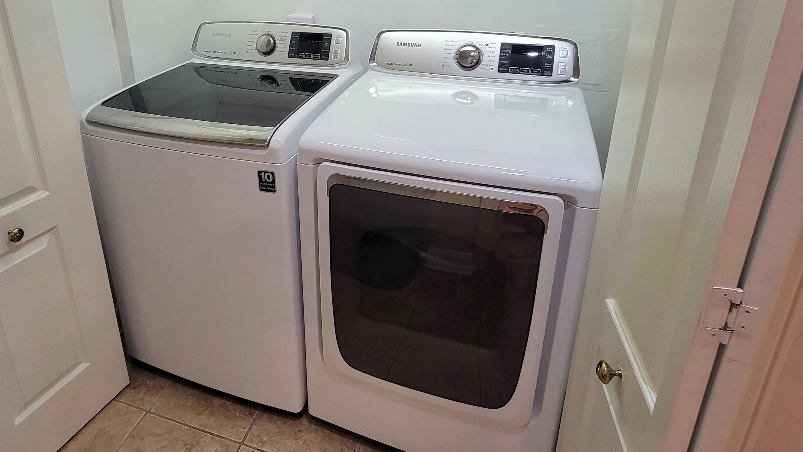 Un appareil compact, blanc, combinant lave-linge et sèche-linge, avec un autocollant indiquant une garantie de 10 ans, situé dans une petite buanderie dotée d’un sol carrelé et d’une porte blanche.
