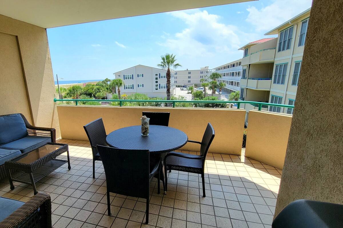 A balcony with a round table and chairs, a sofa, and a view of a building and palm trees.