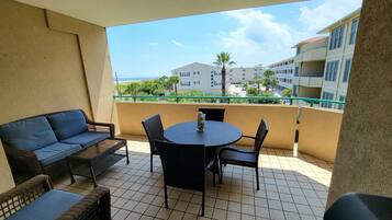 A balcony with a round table and chairs, a sofa, and a view of a building and palm trees.
