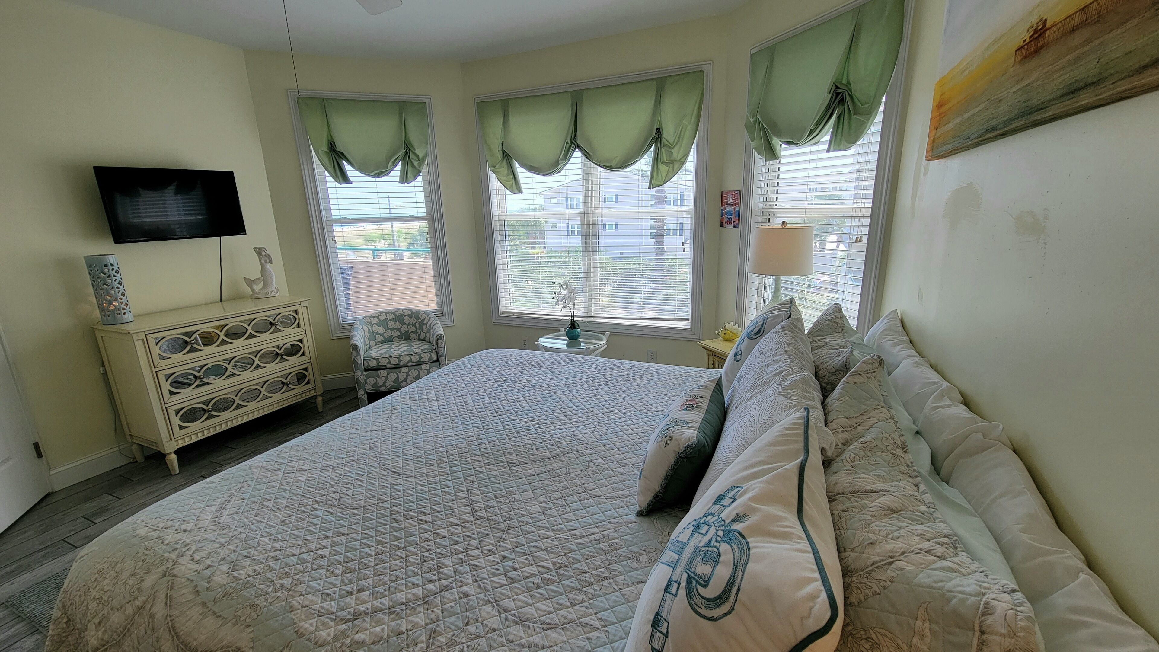 Une chambre à coucher avec un grand lit, une commode, une chaise et un téléviseur fixé au mur.