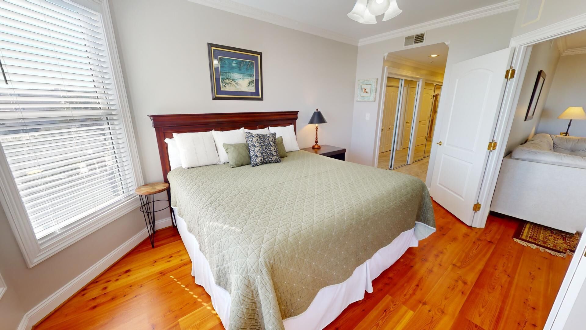 A bedroom with a large bed, wooden flooring, a nightstand with a lamp, and a door leading to a bathroom.