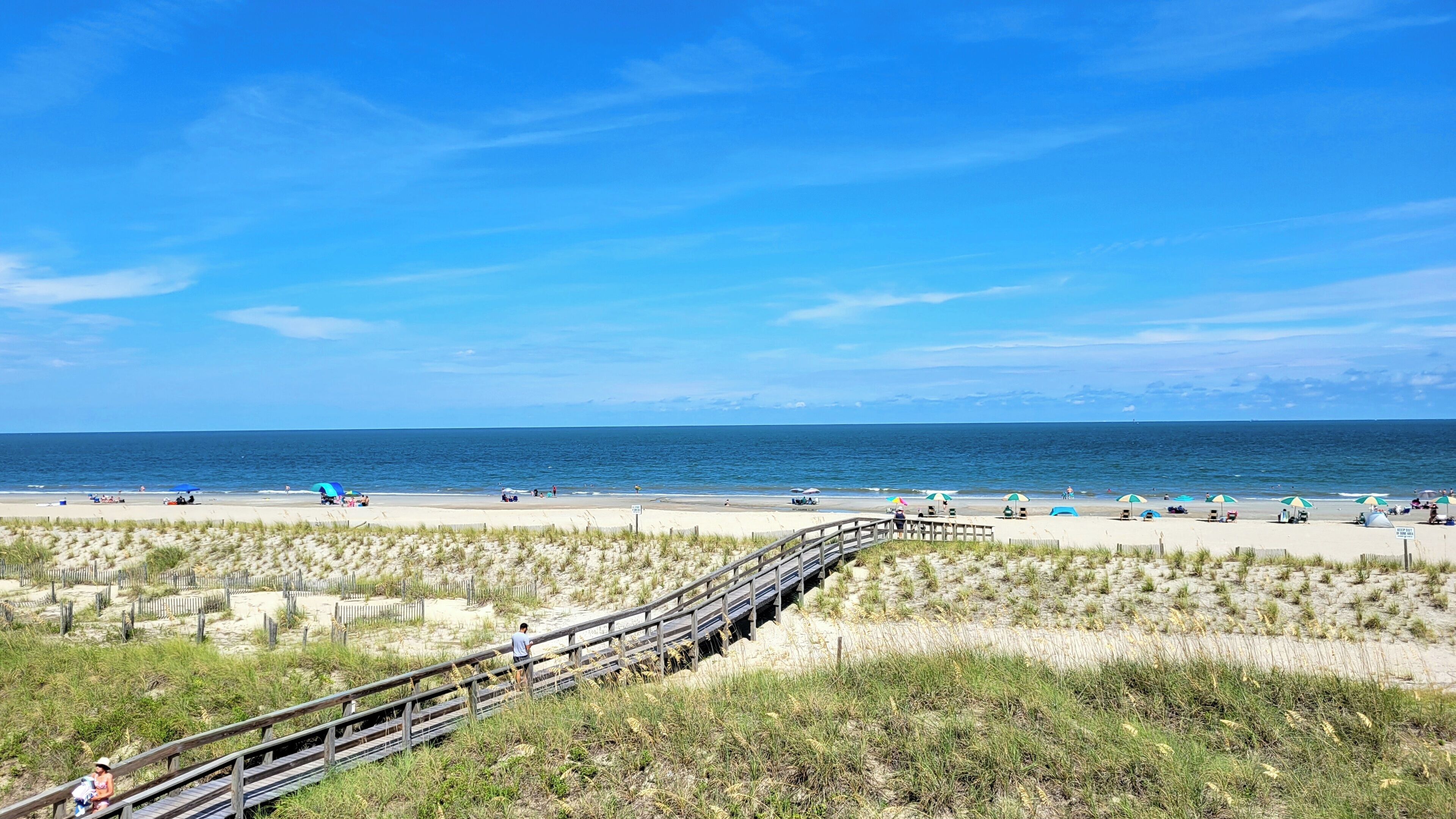 A beach with a wooden boardwalk leading to the shore, sandy dunes, and the ocean.