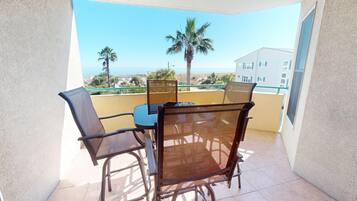A balcony with a table and chairs, overlooking a beach and palm trees.