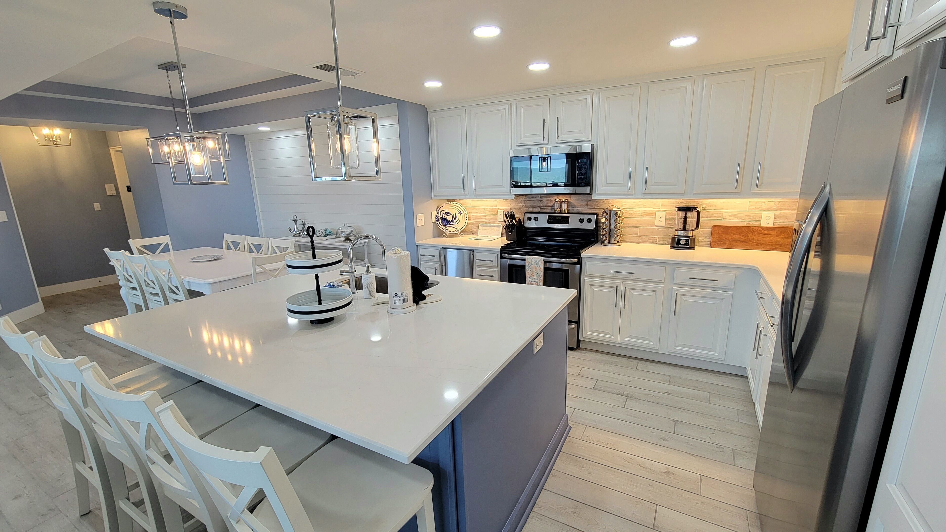 A modern kitchen with white cabinetry, a central island, stainless steel appliances, and pendant lighting.