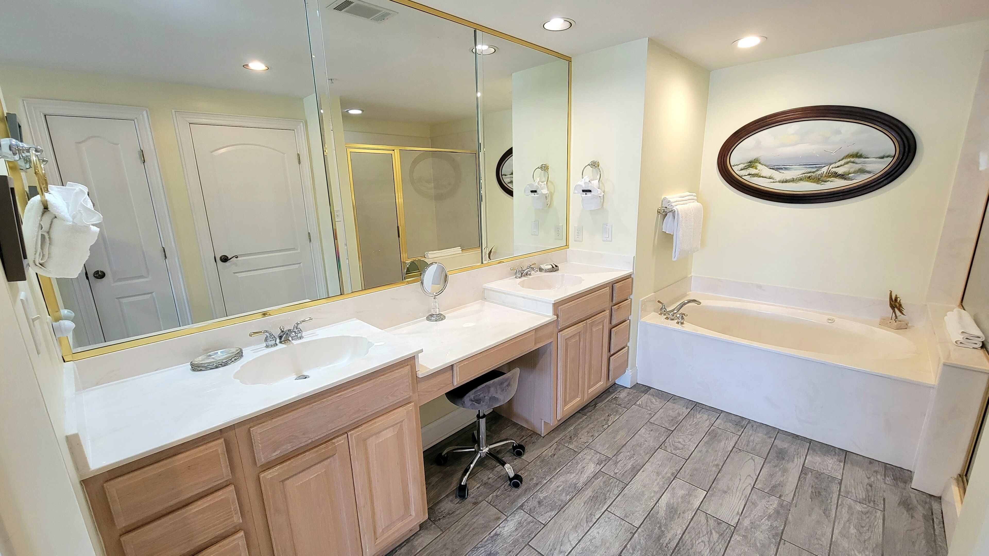 A bathroom with two sinks, a large mirror, a bathtub, and wooden cabinets.