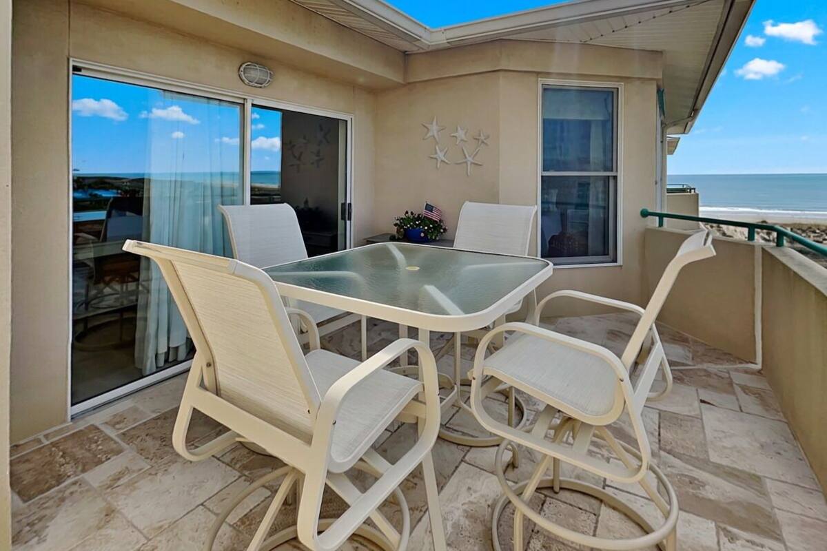 A balcony with a glass table and chairs, a view of the ocean, and a small American flag decoration.
