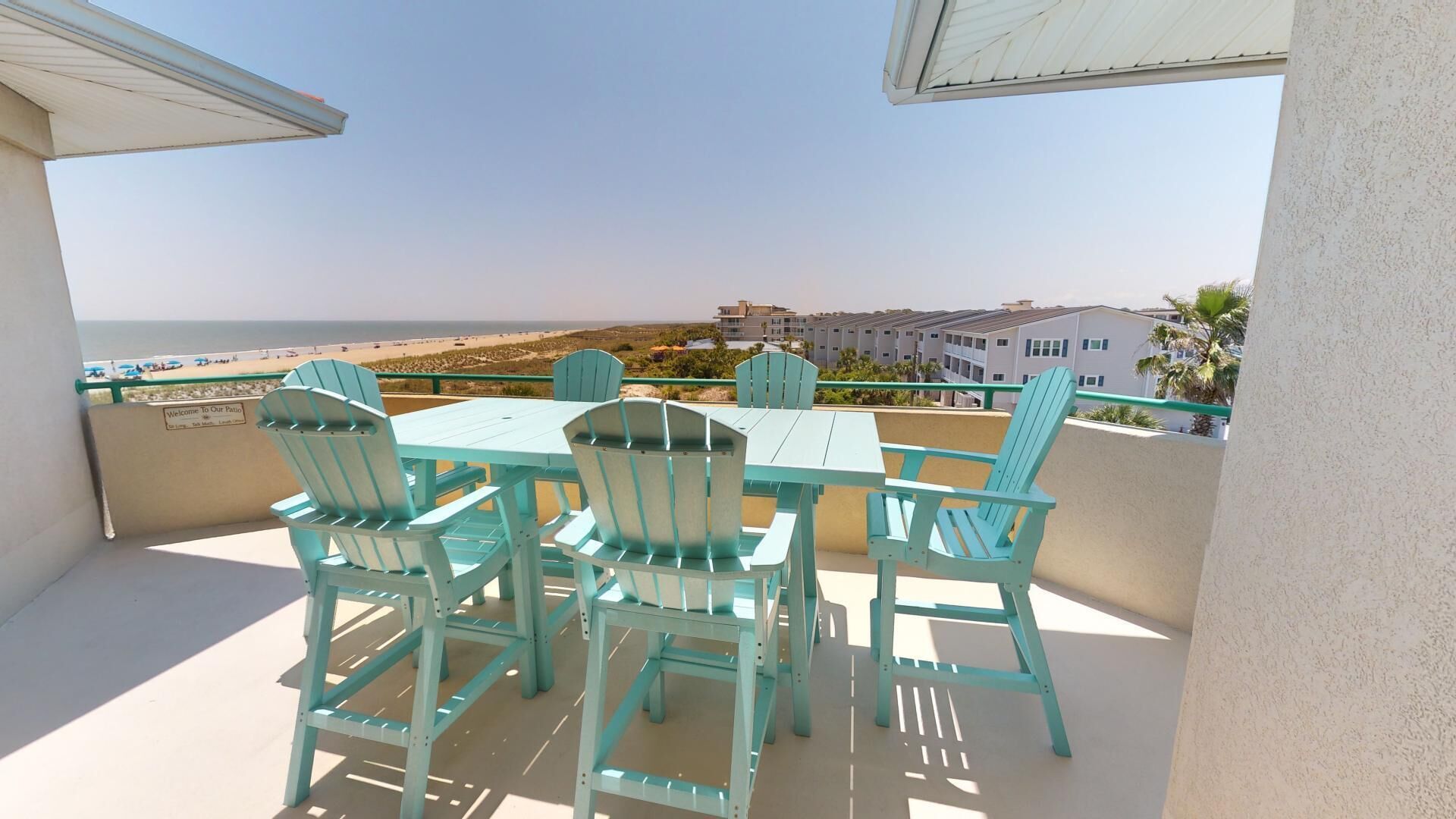 Un balcon avec une table et des chaises, donnant sur une plage et des immeubles.