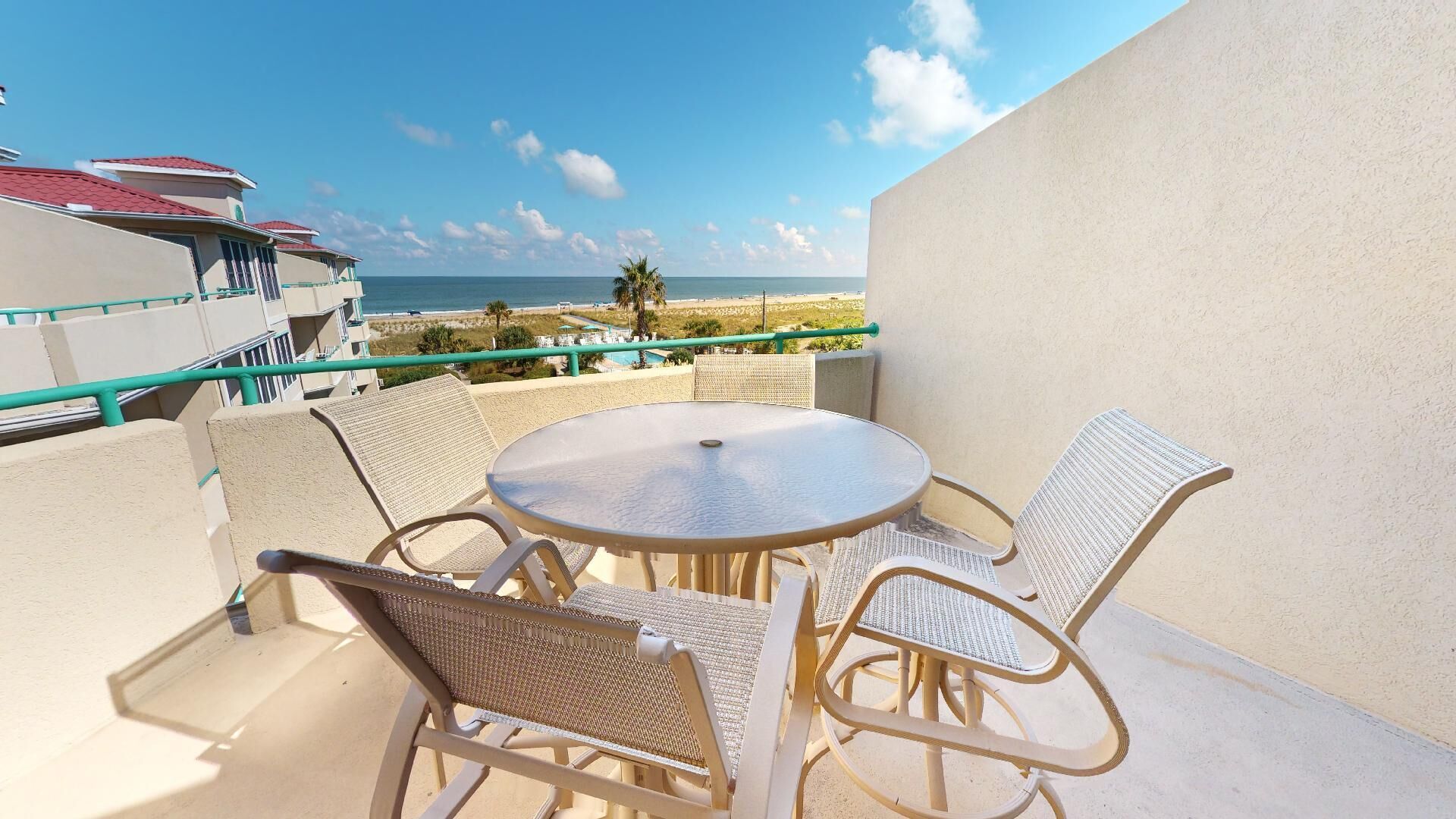 Ein Balkon mit rundem Tisch und vier Korbstühlen, der Blick auf einen Strand und den Ozean geht.