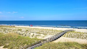 Una spiaggia con una passerella di legno, dune sabbiose e ombrelloni.