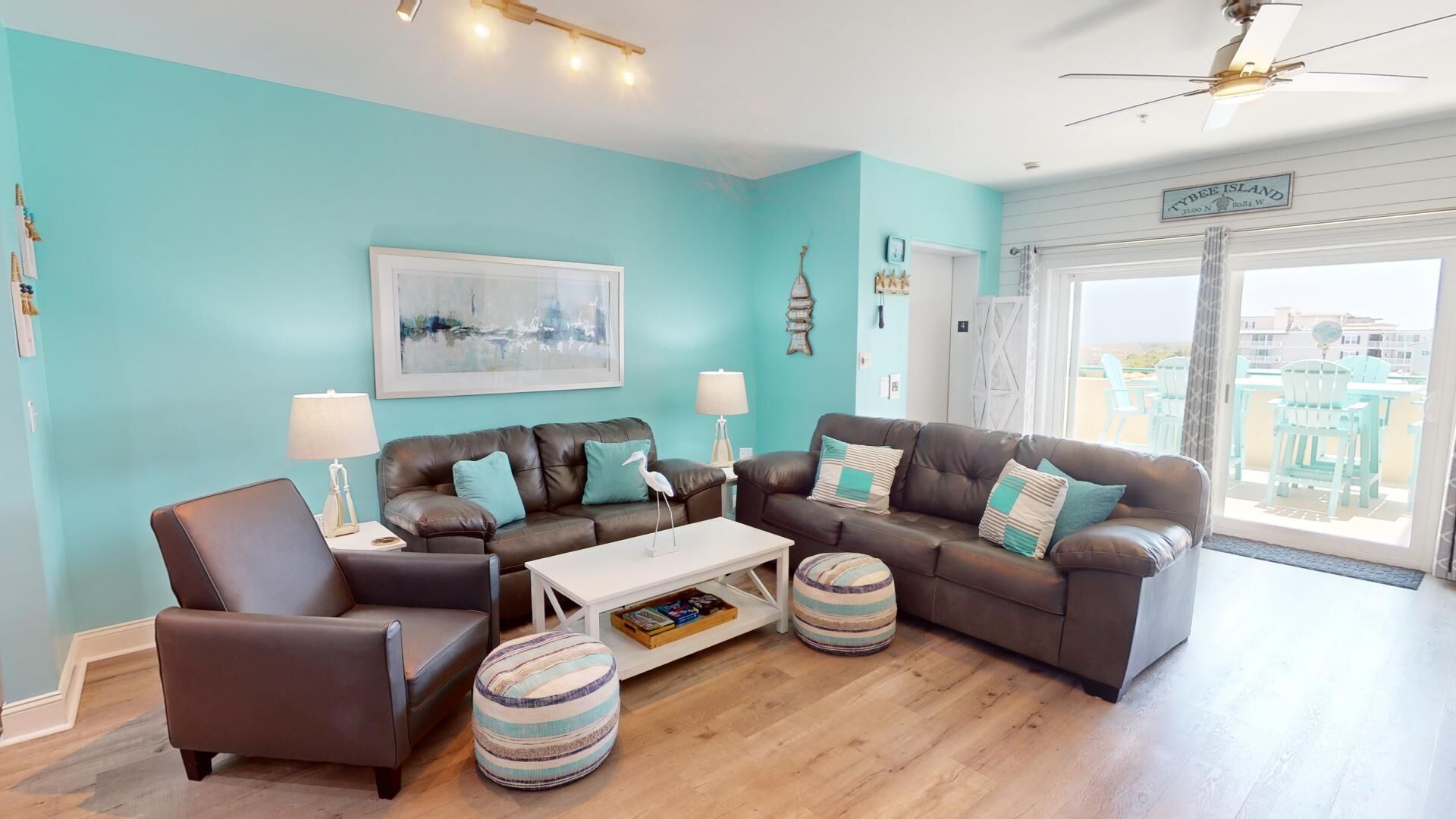 A living room with a teal wall, a brown leather sofa set, a white coffee table, and striped ottomans.