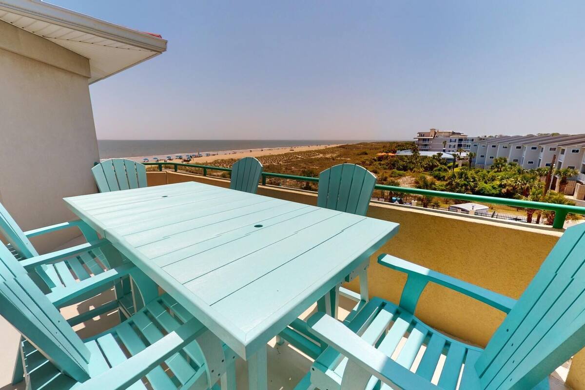 A balcony with a table and chairs, overlooking a beach and a resort area.