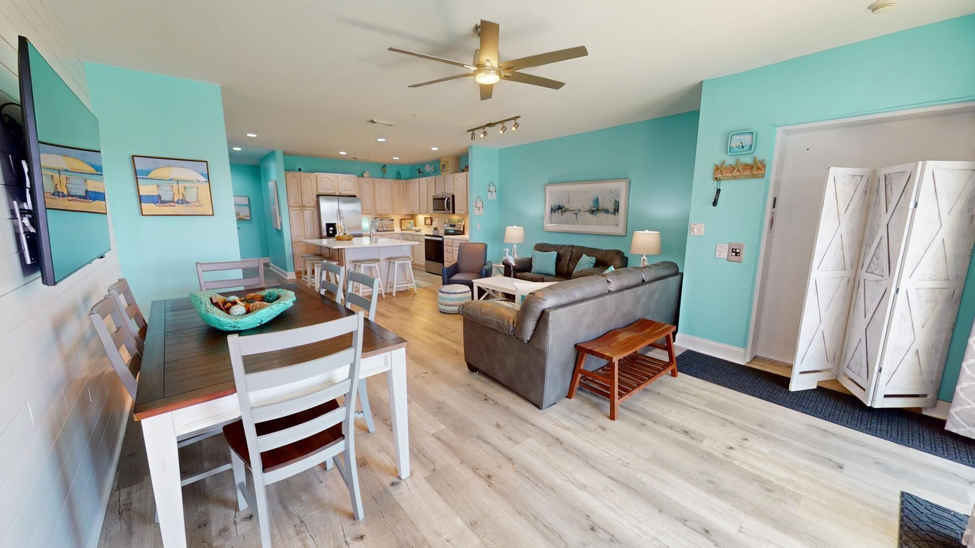 A modern living room with a dining area, a kitchen in the background, and a ceiling fan.