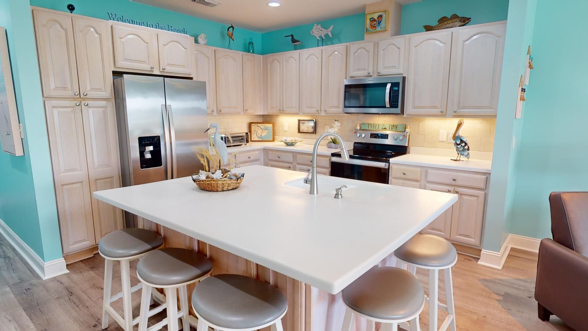 A kitchen with white cabinets, a stainless steel refrigerator, a microwave, and a sink with a modern faucet. There are four stools around the island.