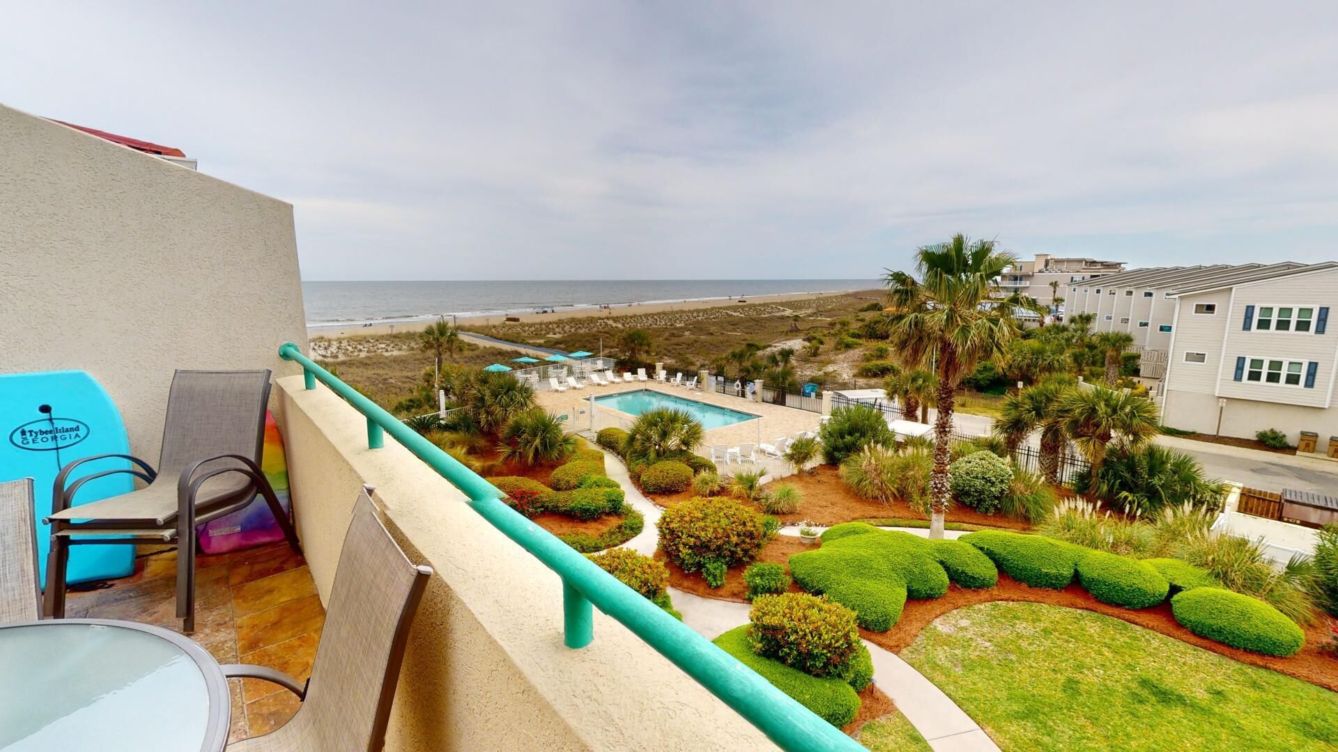Un balcon offrant une vue sur une plage, une piscine et des jardins paysagers soignés.