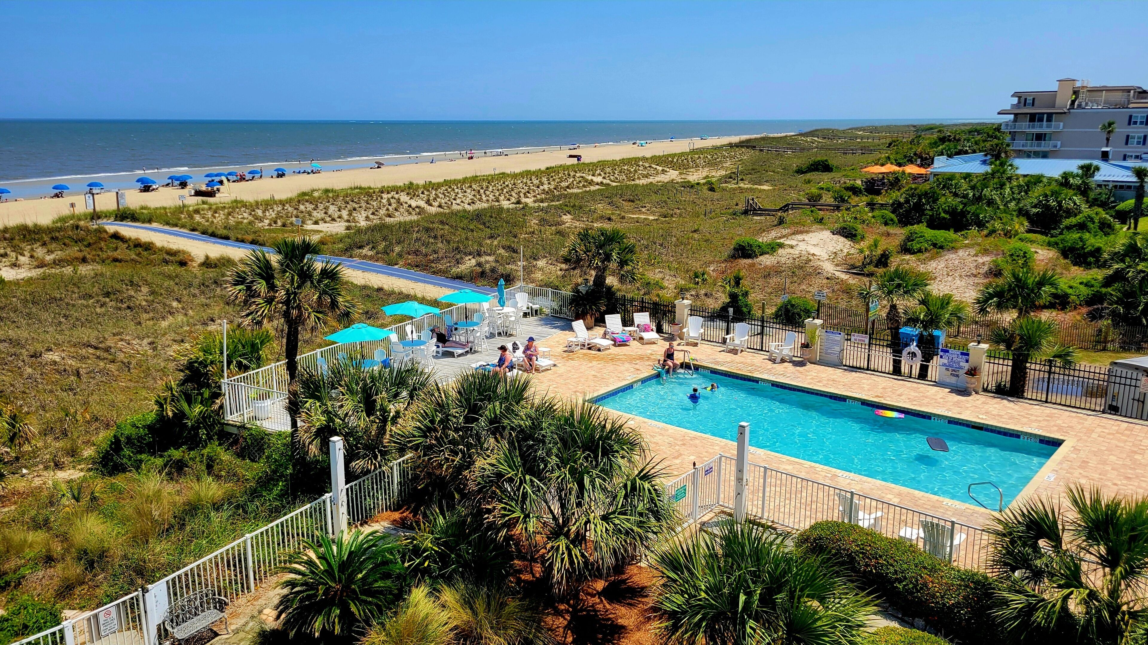 A pool area with a view of the beach, surrounded by palm trees and a fence.