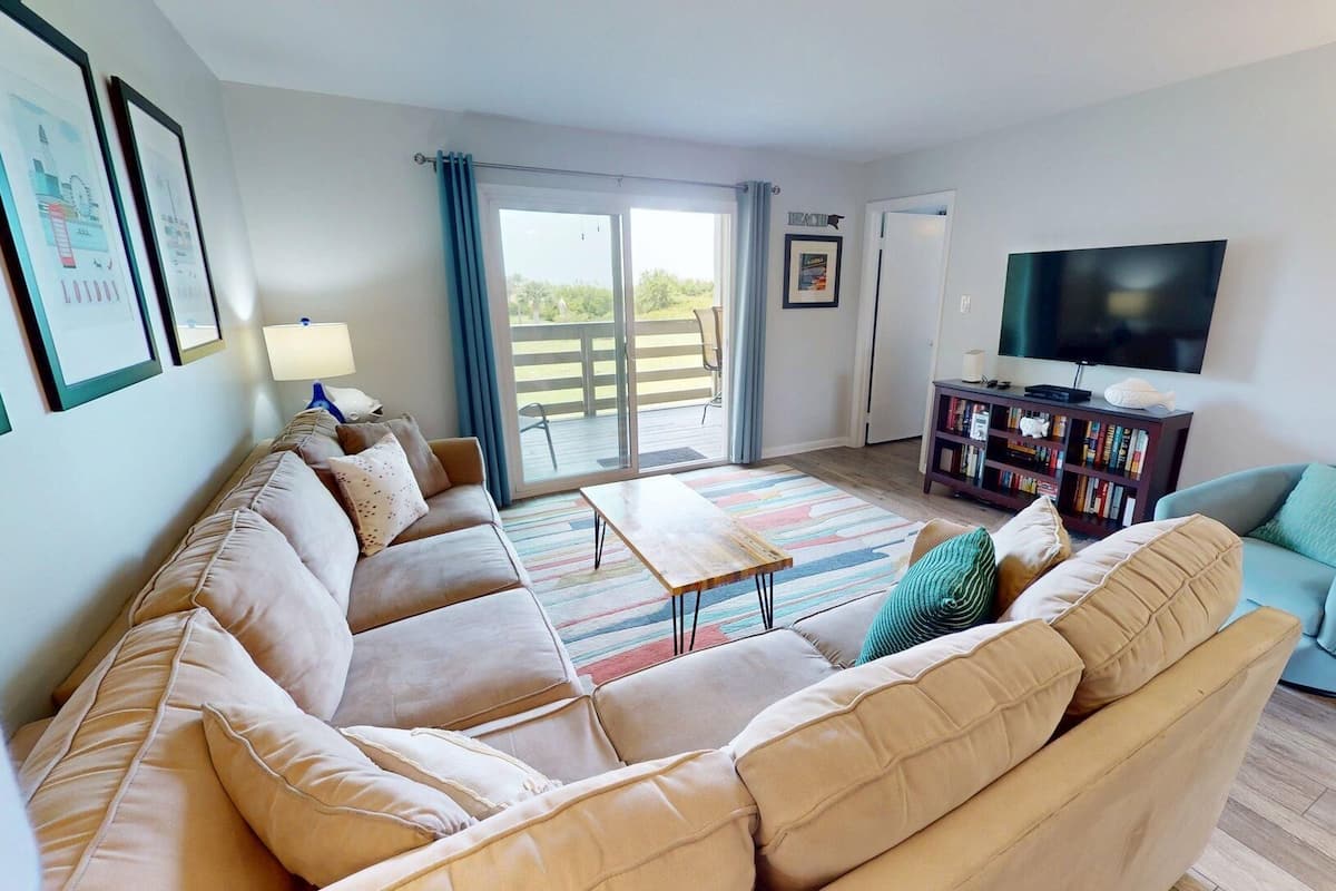A living room with a beige sofa, a blue armchair, a wooden coffee table, a TV, and a bookshelf.