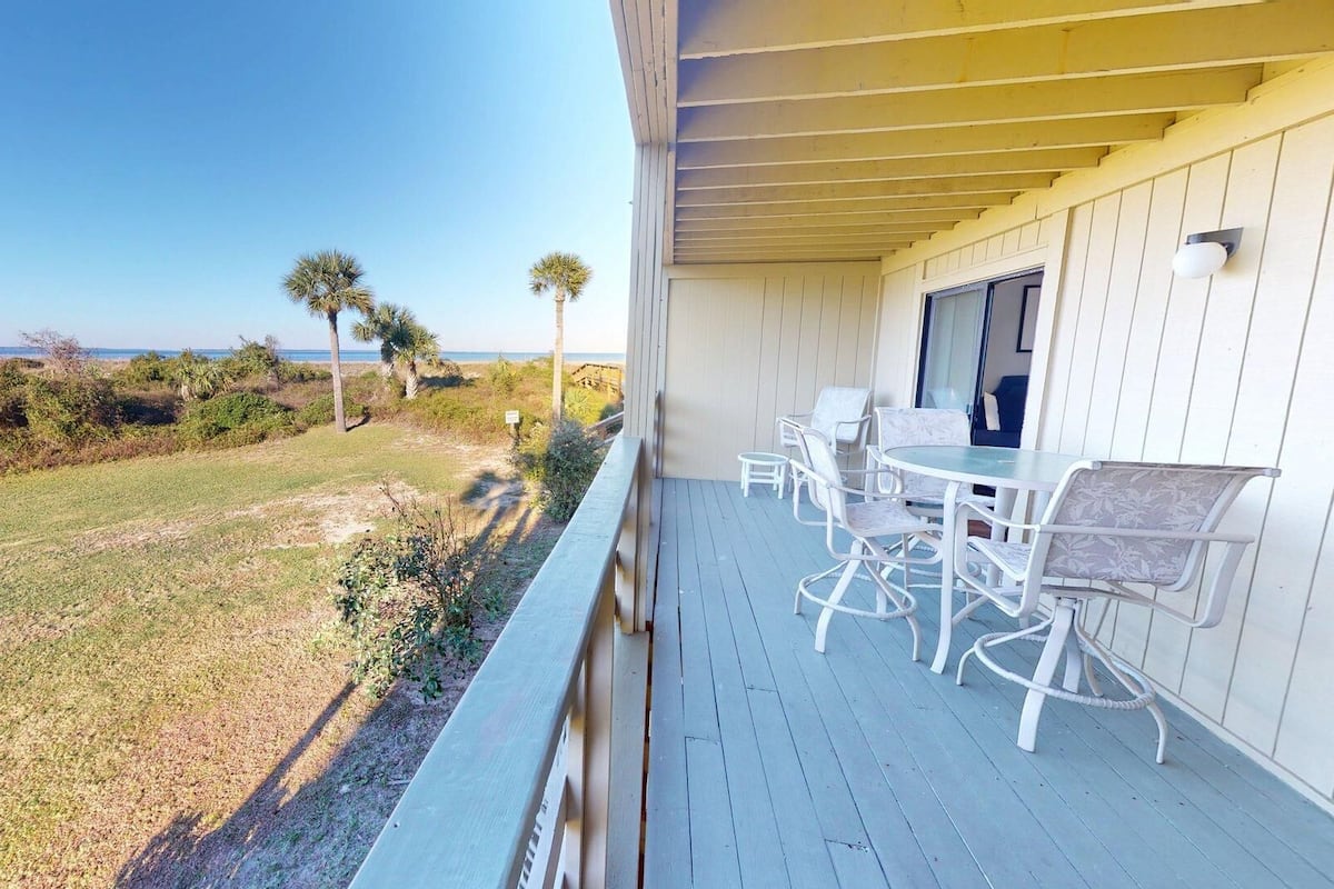 A covered outdoor area with a table and chairs, overlooking a grassy landscape with trees and a view of the ocean.