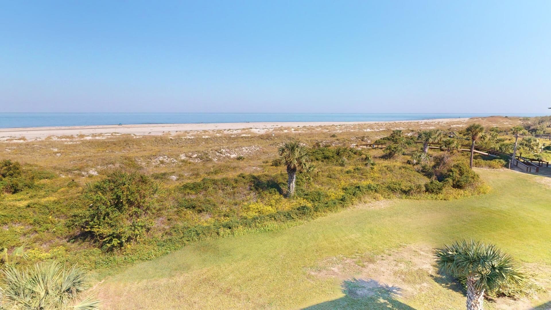 Un paysage côtier comprenant une plage, des zones herbeuses et une végétation clairsemée.