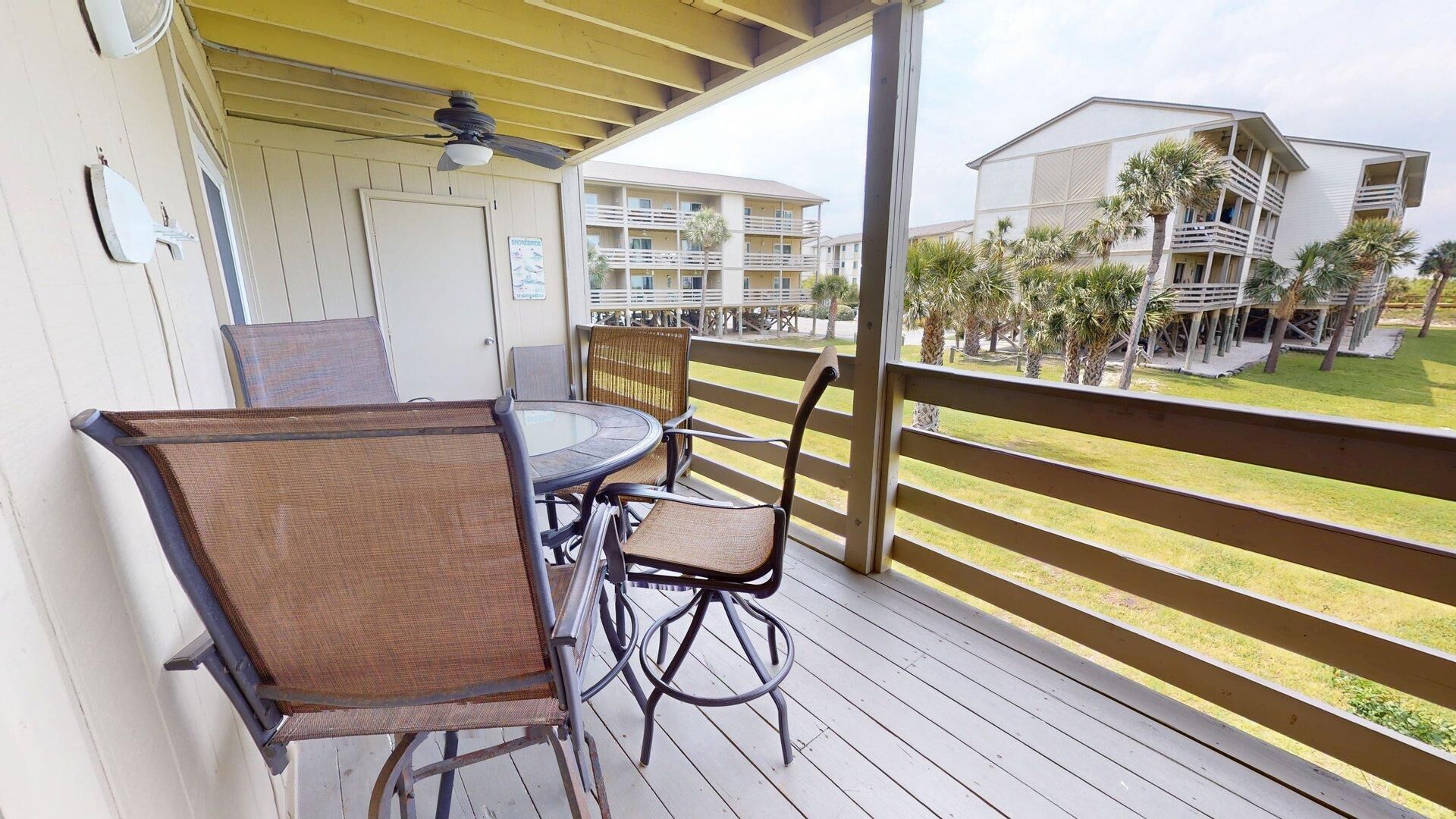 A balcony with a table and chairs, overlooking a pool area with palm trees and a building with balconies.