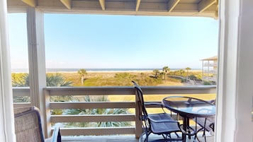 Un balcón con vista a la playa, una mesa y sillas.