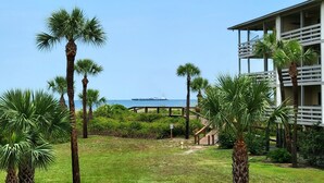 A coastal hotel with palm trees, a view of the sea, and a large ship in the distance. - Lighthouse Point 3 by Tybee Vacation Rentals (Tybee Island)