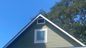 A single-story house with a gabled roof, a front porch with two chairs, and a small window above the door.