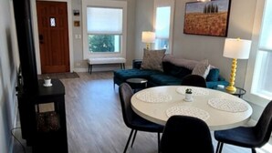 A spacious living area with a round dining table, black chairs, a blue sofa, and a ceiling fan.