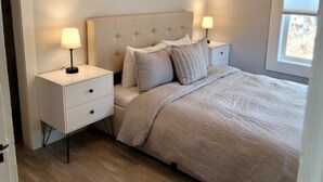 A bedroom with a bed, two bedside tables with lamps, a window, and a ceiling light fixture.
