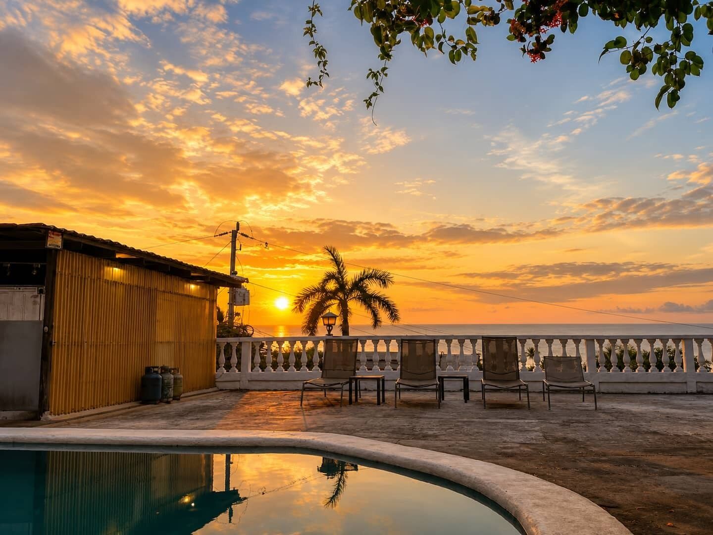 A rooftop pool with a sunset view, a building with a corrugated metal exterior, and a white balustrade.