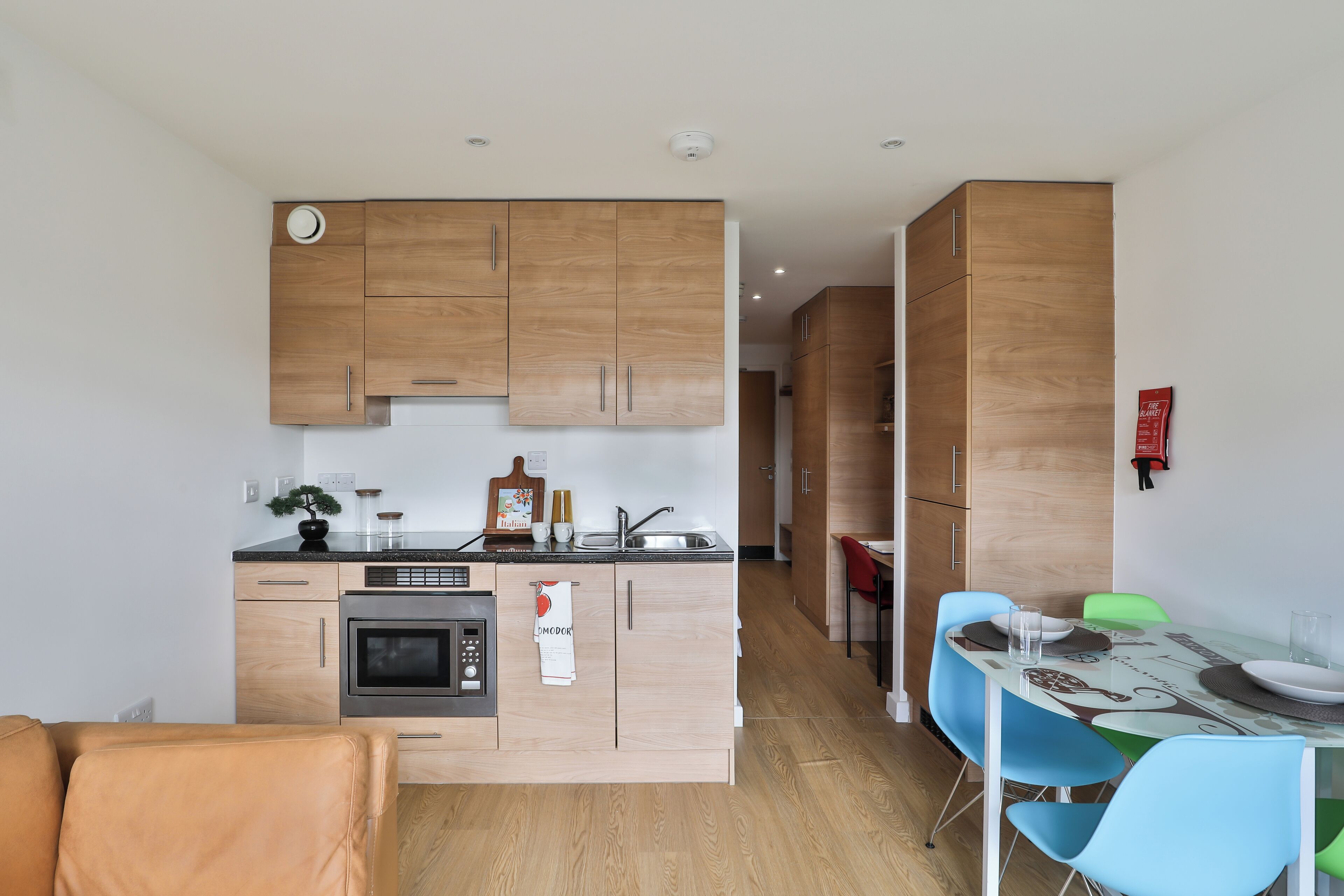A modern kitchen with wooden cabinets, a built-in oven, and a dining area with a table and chairs.