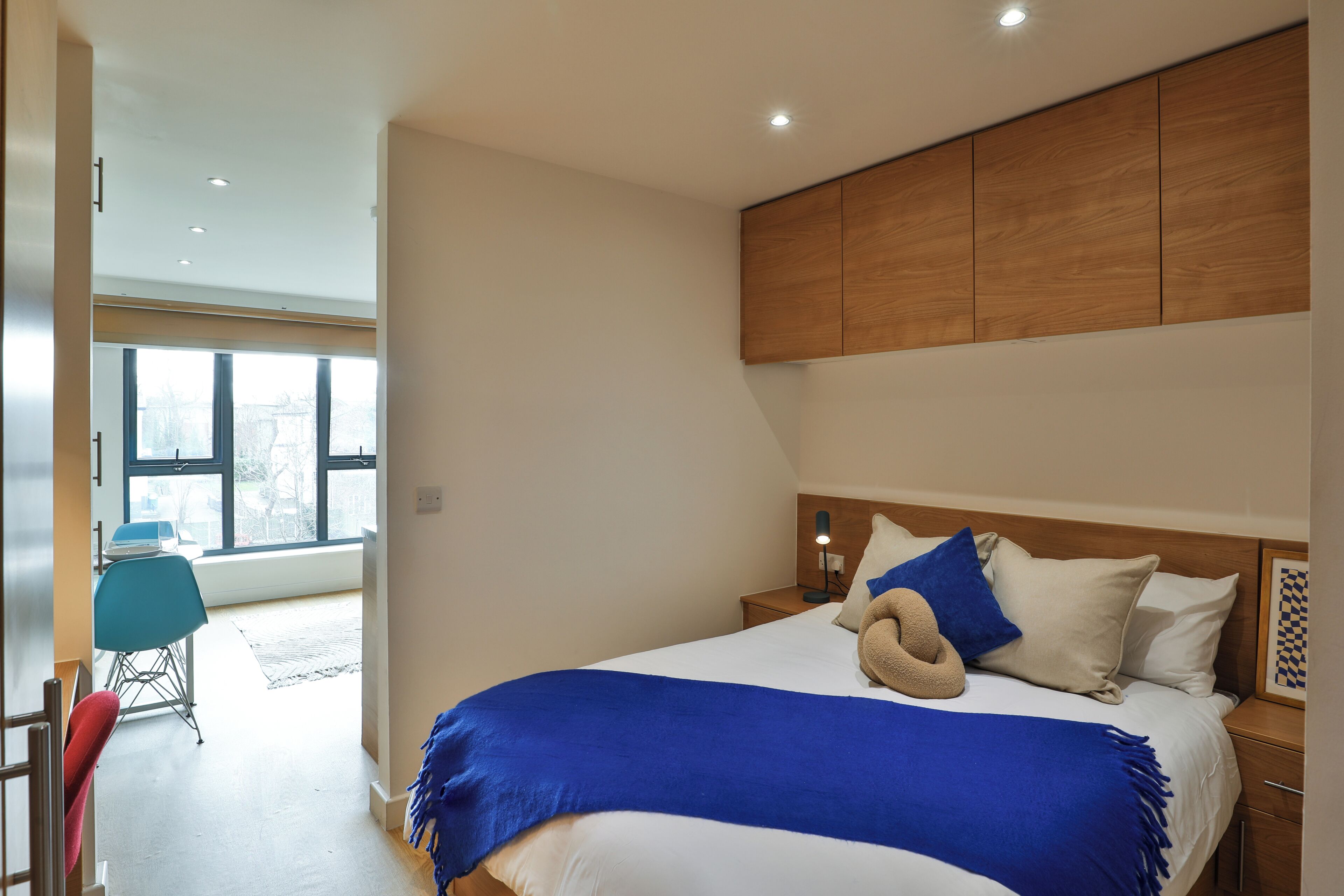 A modern bedroom with a large bed, a wooden headboard, and a view of the outside through large windows.