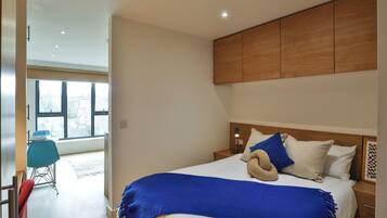 A modern bedroom with a large bed, a wooden headboard, and a view of the outside through large windows.