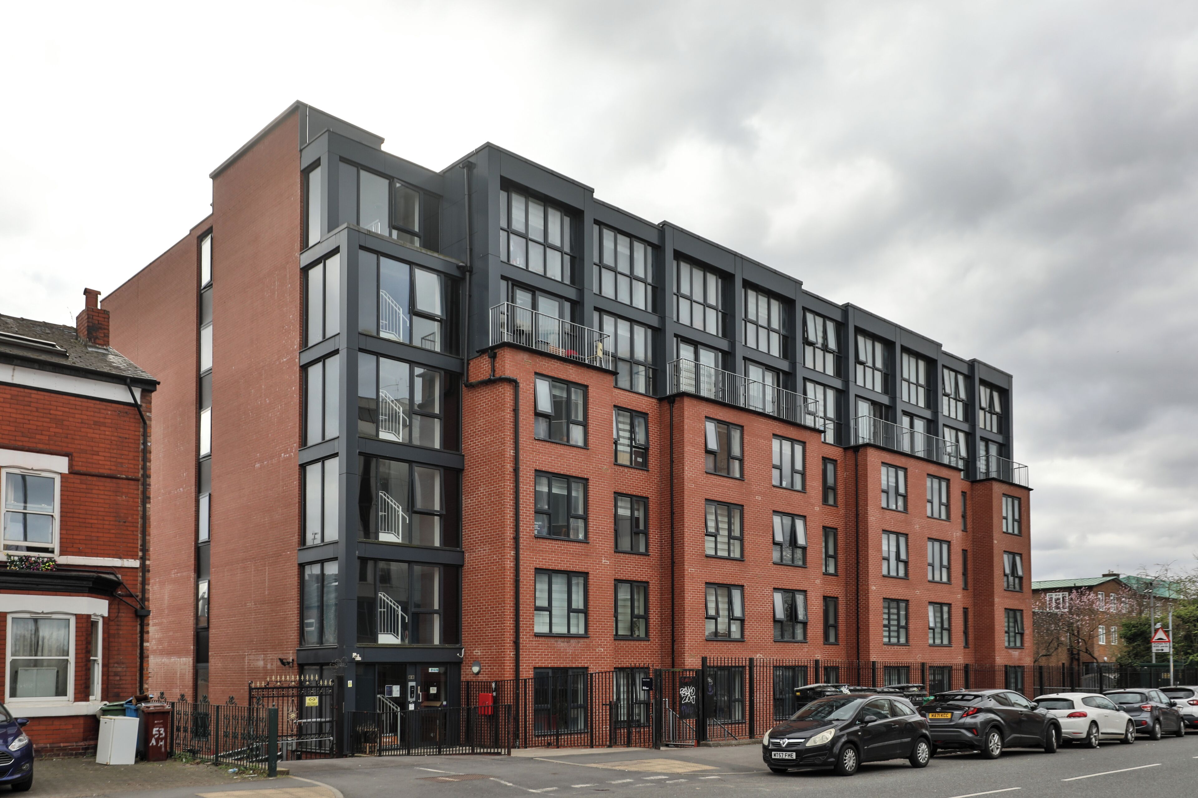 A modern multi-story building with large windows and a parking area in front.