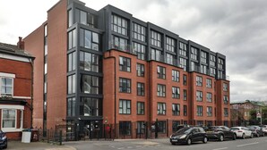 A modern multi-story building with large windows and a parking area in front. - Student Only Tatton House  (Manchester)