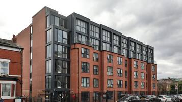 A modern multi-story building with large windows and a parking area in front.