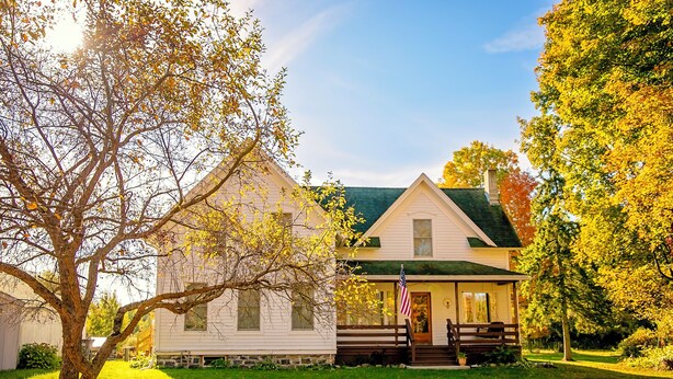 A two-story white house with a green roof, a front porch, and an American flag. - Minutes from SLU, Clarkson, & SUNY schools.  4-bd Family Friendly Farmhouse (Canton)