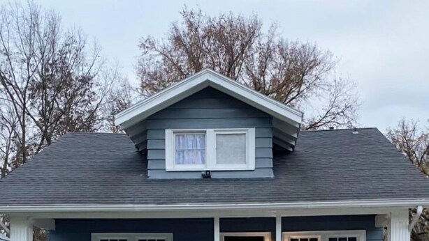A two-story house with a front porch, stone foundation, and a dark gray roof.
