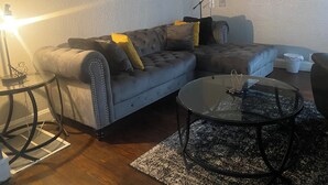 A modern living room with a grey sofa, a glass coffee table, and a wall-mounted TV.