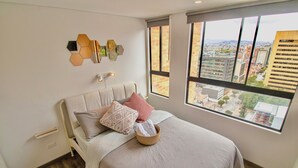 A modern bedroom with a large window, a bed with multiple pillows, a bedside table, and a wall-mounted light fixture. - Downtown Bogotá | Work & Stay (Bogotá)