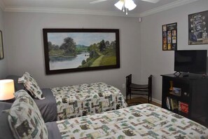 A bedroom with two beds, a TV, a bookshelf, and a painting of a landscape.