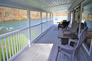 Une véranda couverte avec des balustrades blanches, une table et plusieurs fauteuils Adirondack donnant sur une rivière.
