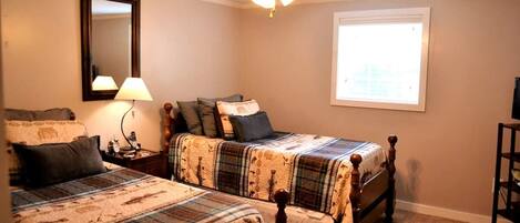 A bedroom with two wooden beds, a ceiling fan, a nightstand with a lamp, a mirror, and a window with blinds.