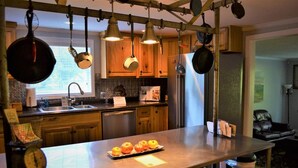 A kitchen with wooden cabinets, hanging pots, a stainless steel refrigerator, and a central island with fruits. - Riverview Retreat Pad #5 (Bristol)
