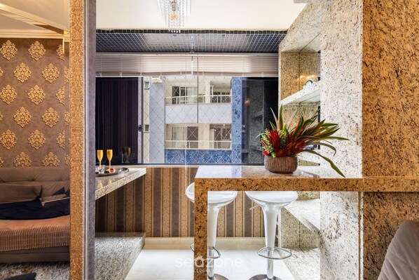 A modern kitchen with a marble countertop, two bar stools, and a potted plant.